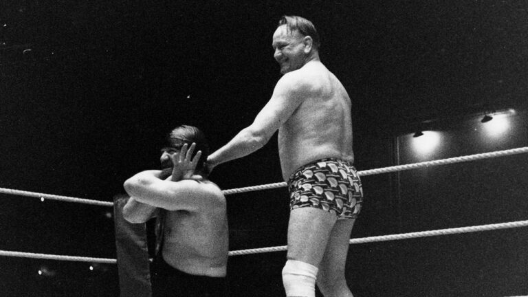 A black and white photo of Les Kellett in hedgehog-patterend trunks, grabbing another wrestler by the wrist.