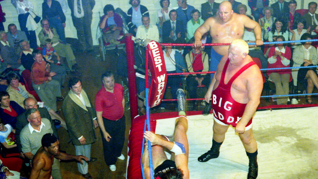 Big Daddy throws a wrestler out of the ring as Mal "King Kong" Kirk watches on on the apron.